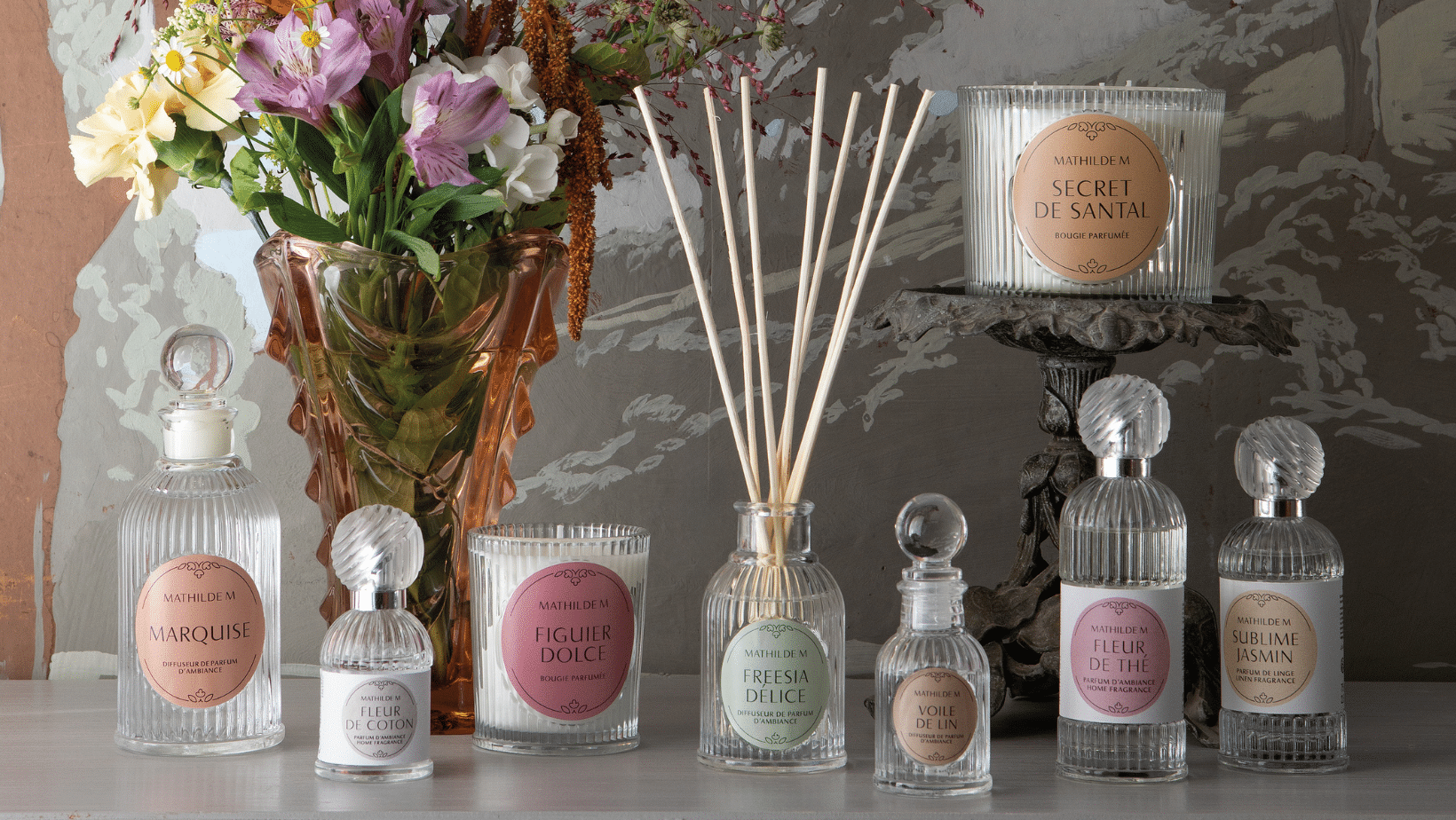 Elegante sfeerfoto van Mathilde M geurkaarsen, geurstokjes en huisparfums in glazen flacons op een tafel met bloemen